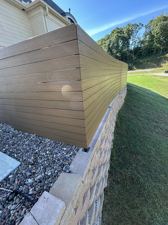 A modern composite fence installed on top of a stone retaining wall by Timber Wolf Fence Co. in Rogers, AR.