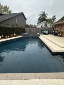 A modern swimming pool with a dark bottom finish and an integrated spa, completed by I10 Pool Plastering LLC in Kenner, LA.