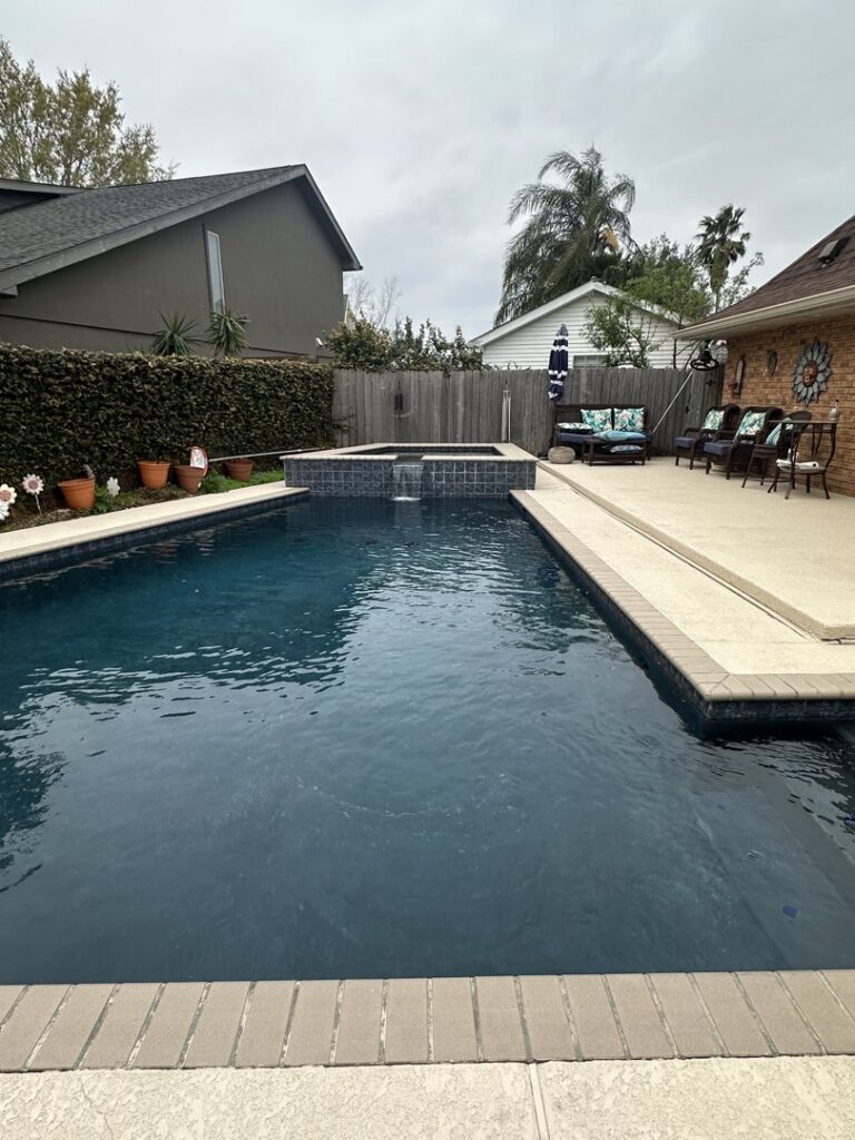 A modern swimming pool with a dark bottom finish and an integrated spa, completed by I10 Pool Plastering LLC in Kenner, LA.