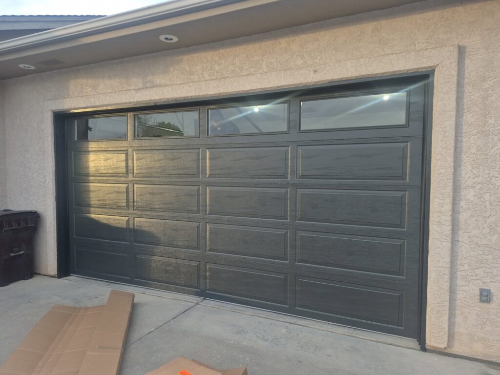 A close-up view of a modern dark grey garage door with top windows, installed by Prutch's Garage Door in Colorado Springs, CO.
