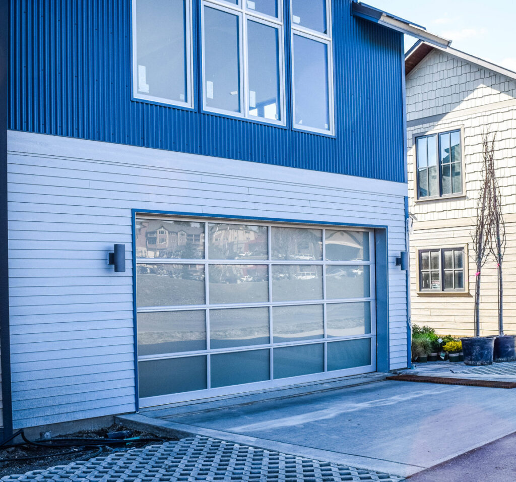Modern full-view glass garage door on a blue and white contemporary home, installed by Continental Door Company, Spokane Valley, WA.