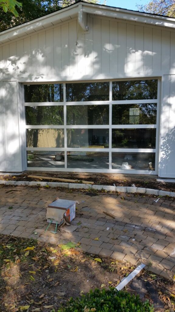 A modern full-view glass garage door installed on a residential home by Garage Door Specialists Of Oklahoma Inc. in Midwest City, OK.