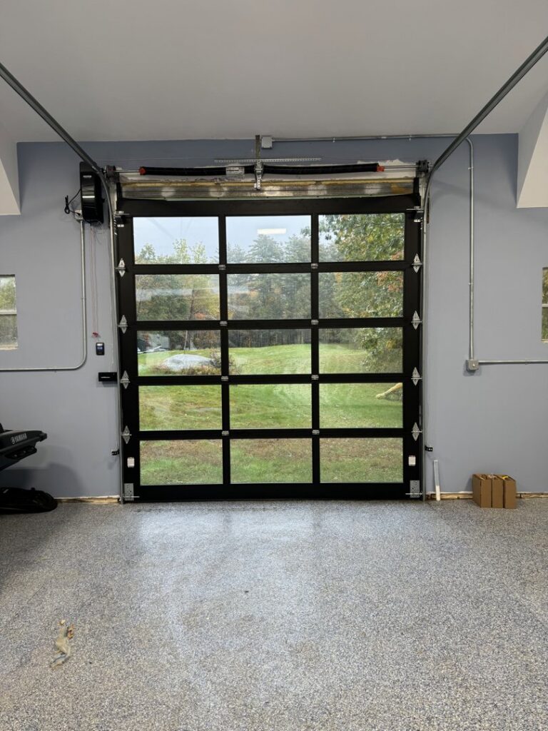 Interior view of a garage featuring a modern black full-view glass garage door installed by PM Garage Door in Hudson, NH.