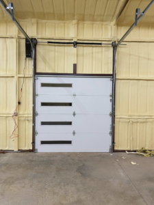Exterior view of two modern brown garage doors with illuminated windows at dusk, installed by Okie Garage Door Specialist in Tulsa, OK