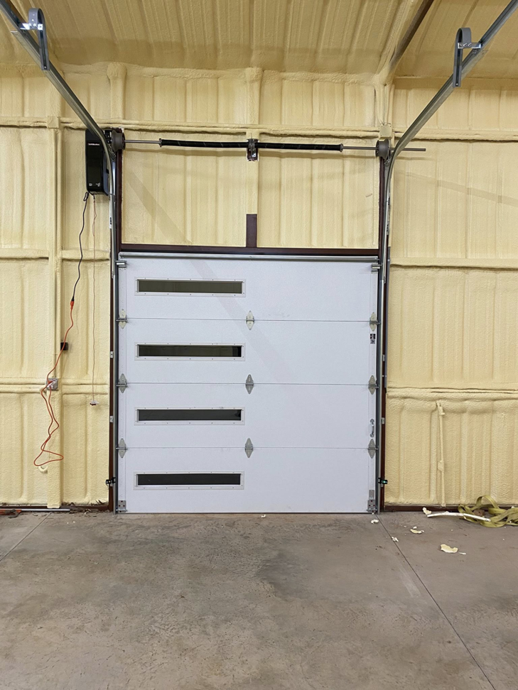 Exterior view of two modern brown garage doors with illuminated windows at dusk, installed by Okie Garage Door Specialist in Tulsa, OK