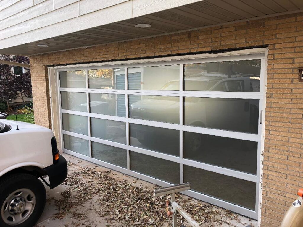 A modern glass garage door installed on a residential garage, showcasing services by Madison Overhead Garage Door Services in Madison, WI.