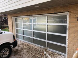 A modern glass garage door installed on a residential garage, showcasing services by Madison Overhead Garage Door Services in Madison, WI.