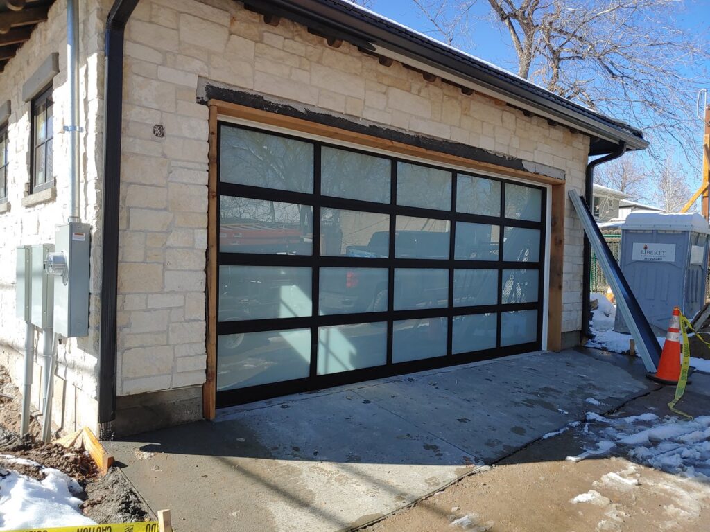 Installation of a modern glass panel garage door on a stone house by Colorado Garage Door Pro's in Denver, CO