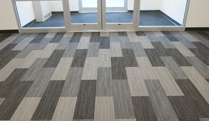 A modern grey and black patterned carpet tile installation leading to glass doors by Direct Solutions Flooring in Baltimore, MD.
