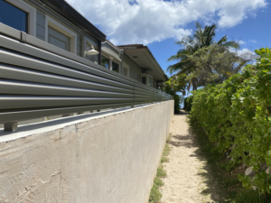A modern horizontal slat fence installed along a sandy path by KunkelWorks Hawaii in Mililani, HI.