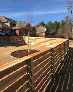 A modern horizontal slat wood fence installed around a tree in a backyard by Alabama's Fencing in Huntsville, AL.