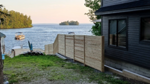 A modern horizontal slat wooden fence installed next to a lakeside home by Creative Fence in Casco, ME.