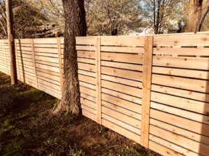 A modern horizontal wood slat fence installed around a tree by Render Fences in Fishers, IN.