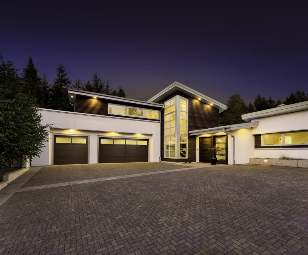 A modern house with two dark brown garage doors, illuminated at dusk, installed by Lifetime Door Company in Brookfield, WI.