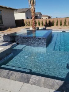A modern completed pool with a raised spa featuring dark tile and a palm tree by EZ POOL Solutions in Tucson, AZ