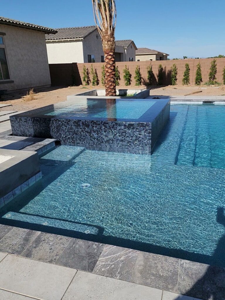A modern completed pool with a raised spa featuring dark tile and a palm tree by EZ POOL Solutions in Tucson, AZ