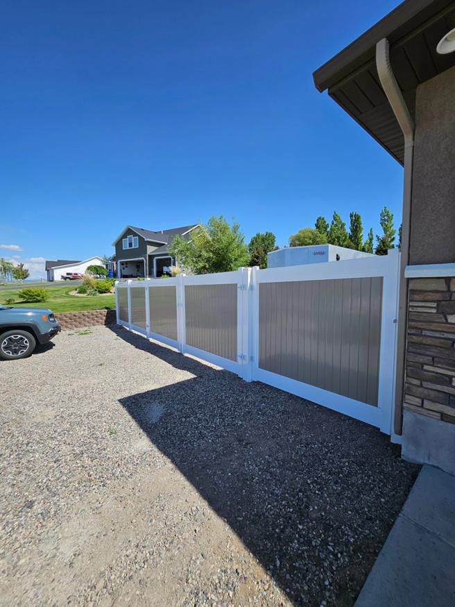 A modern two-tone privacy fence with a gate installed along a gravel driveway by Performance Fencing in Rigby, ID.
