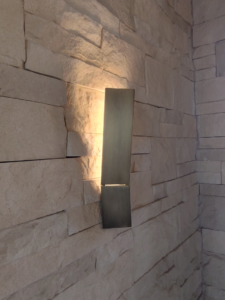 A modern wall sconce light fixture installed on a stone wall by Ryco Electric in York, PA