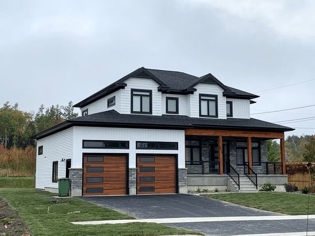 A modern white house showcasing two contemporary wooden garage doors with horizontal panels, installed by Monroe Overhead Doors in Monroe, LA.