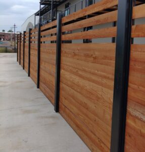 A modern wooden fence with black metal posts installed along a sidewalk by Kelley Fence and Gate in Eva, AL.