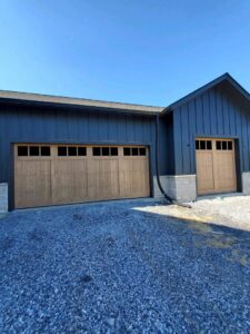 Two modern wood-look garage doors with windows installed on a dark-sided building by Door Serv Pro in Inwood, WV.