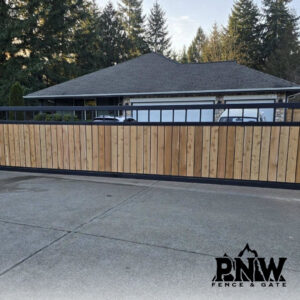 A modern wood and black metal sliding gate providing privacy for a residential property, installed by PNW FENCE in Lewiston, ID.