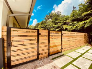 A modern wooden fence with black metal posts and a gate installed in a tropical setting by Miami Fence Installation Contractors in Miami, FL.
