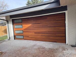 A modern wooden-style garage door with horizontal windows installed by Strongdoor garage in Denver, CO.