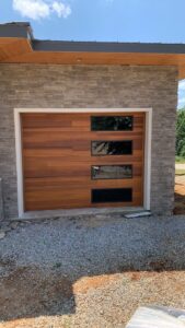 A modern wooden panel garage door with horizontal windows installed by Signature Garage Doors in Huntsville, AL.