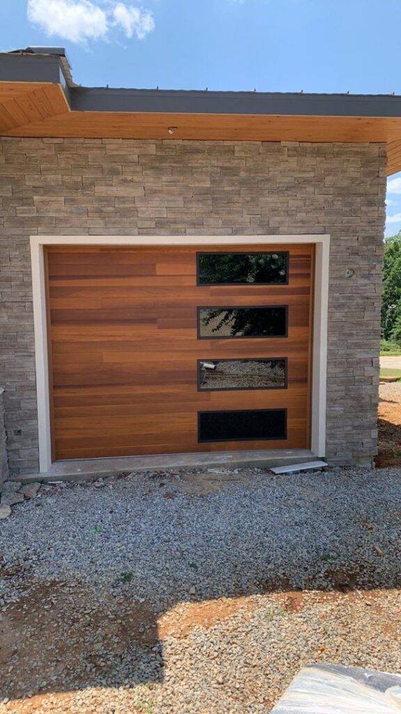 A modern wooden panel garage door with horizontal windows installed by Signature Garage Doors in Huntsville, AL.
