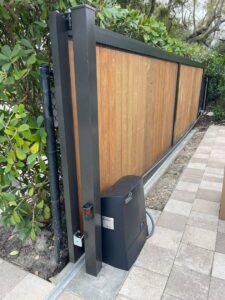 A modern wooden-panel sliding gate with a gate operator motor installed by Motor & Fence Solutions in Miami, FL.