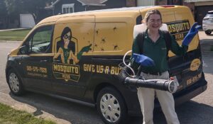 A smiling Mosquito Hero female technician with a backpack sprayer stands by a branded service van in Champaign, IL.