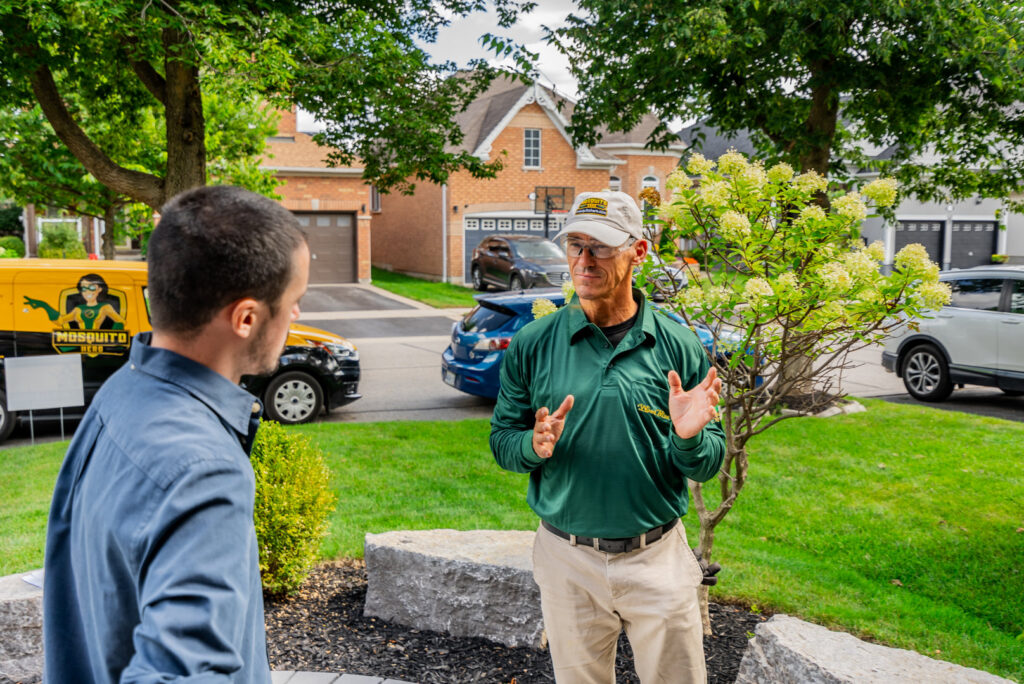 A Mosquito Hero technician discusses pest control services with a customer in a residential area of Champaign, IL.