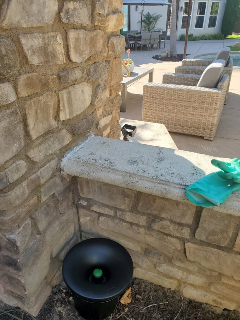 A Mosquito Joe mosquito trap installed on the ground next to a stone wall in Encinitas-Del Mar, San Diego, CA.