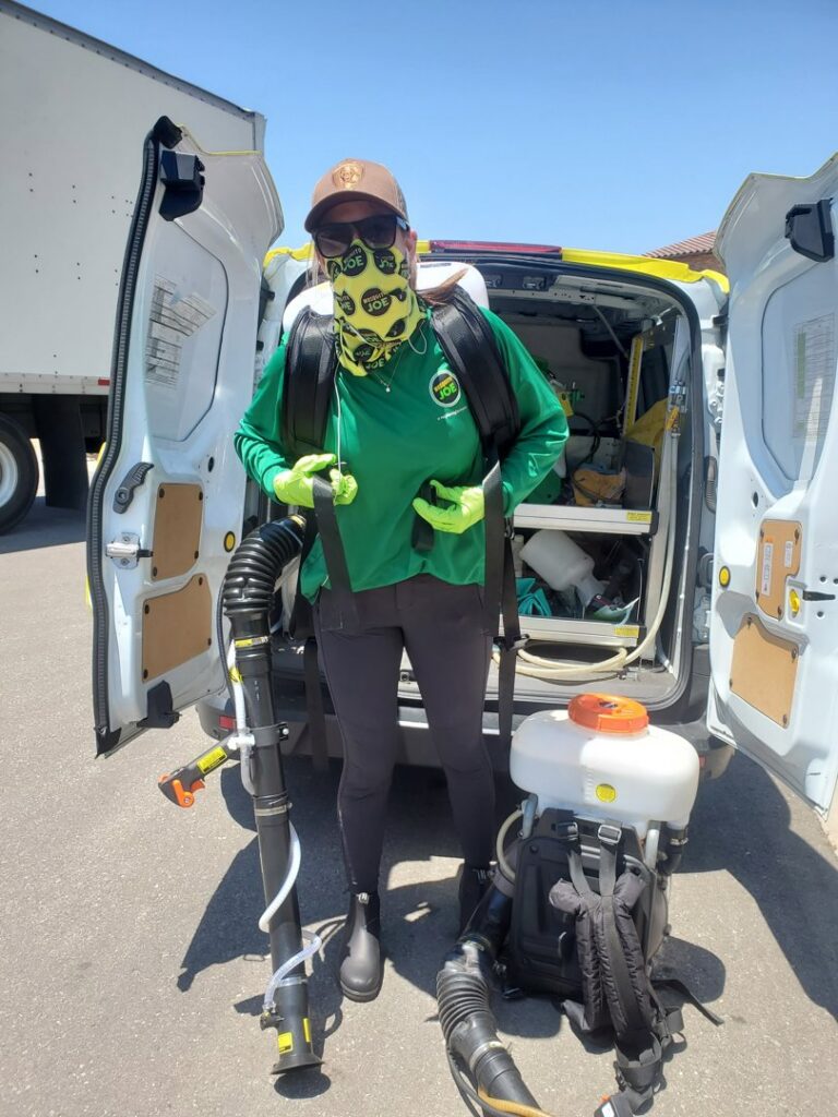 A Mosquito Joe technician with a face covering and pest control equipment standing by a branded van in Encinitas-Del Mar, San Diego, CA.