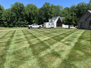 A perfectly mowed lawn with a crisscross pattern, featuring a C&R Lawn Care and Property Services truck and trailer in Evansville, IN.