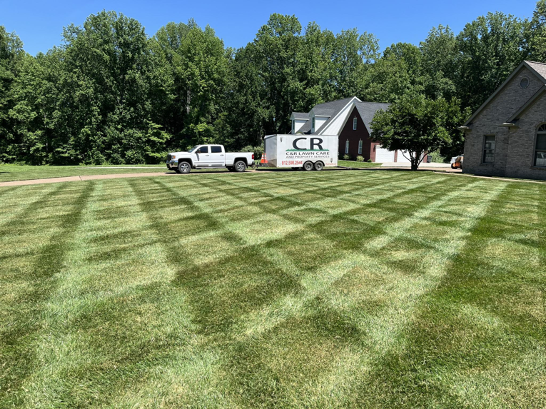 A perfectly mowed lawn with a crisscross pattern, featuring a C&R Lawn Care and Property Services truck and trailer in Evansville, IN.