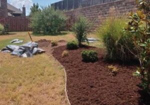 A newly mulched flower bed with bags of mulch nearby, showing landscaping work by From The Roots Lawn Service in Edmond, OK.