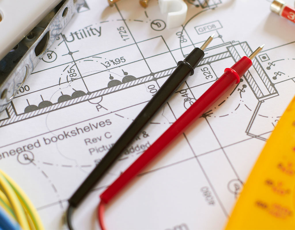 Multimeter probes and other electrical tools laid on blueprints for a project by OMR Electrical Contractors Inc. in Cape Coral, FL.