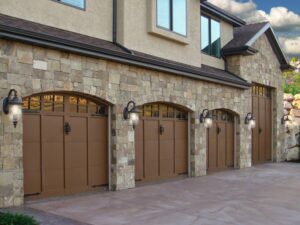 Multiple brown garage doors with arched windows and a stone facade, showcasing an installation by Above The Rest Garage Door in Colorado Springs, CO.