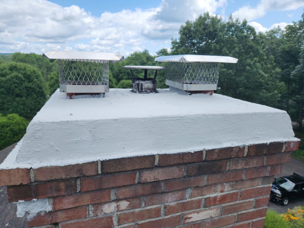 Multiple chimney caps installed on a brick chimney on a roof by Top Dog Hearth Repair & Maintenance, LLC in Worcester, MA