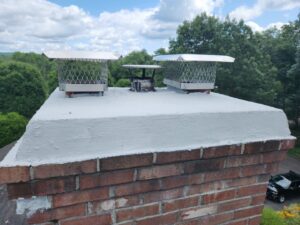 Multiple chimney caps installed on a brick chimney on a roof by Top Dog Hearth Repair & Maintenance, LLC in Worcester, MA