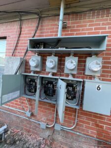 Multiple electrical meters and open service panels showing wiring and breakers on a brick wall, installed by LOJ Electric, LLC in Houston, TX.
