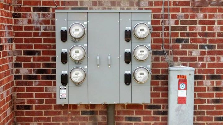Multiple electrical meters and service panels installed on a brick wall by Volt Doctors in Durham, NC