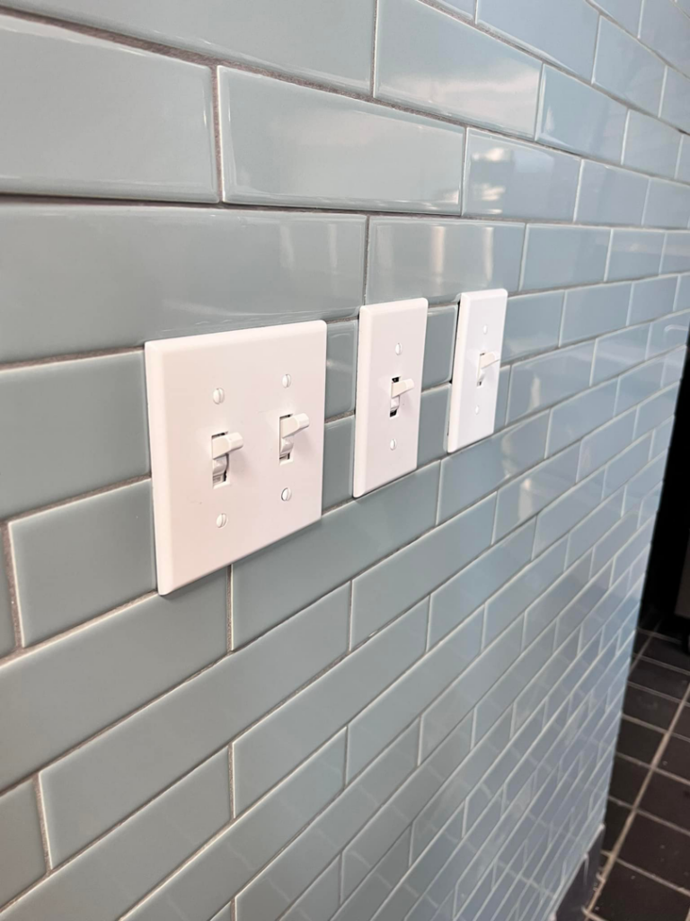 Multiple light switches neatly installed on a light blue tiled wall by Solution Electric in Houston, TX.