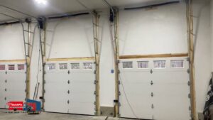 Interior view of a garage showcasing multiple newly installed white garage doors with windows by QuickFix Garage Door Service in Brighton, MA.