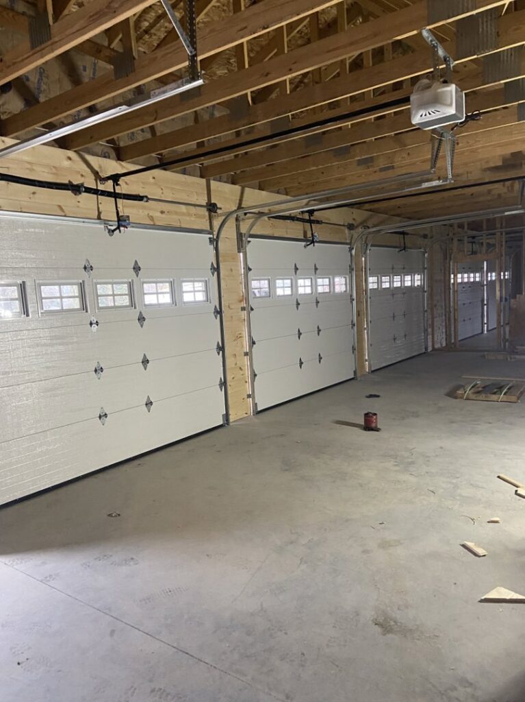 Interior view of a new construction garage with multiple white garage doors recently installed by Garage Door Repair Company, LLC in Pueblo, CO.