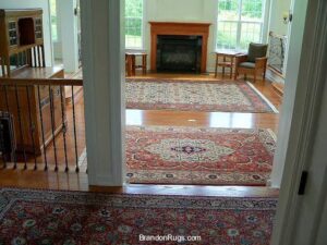 Multiple oriental rugs laid out on hardwood floors in an open-plan area leading to a fireplace, by Brandon Oriental Rugs, Furlong, PA.