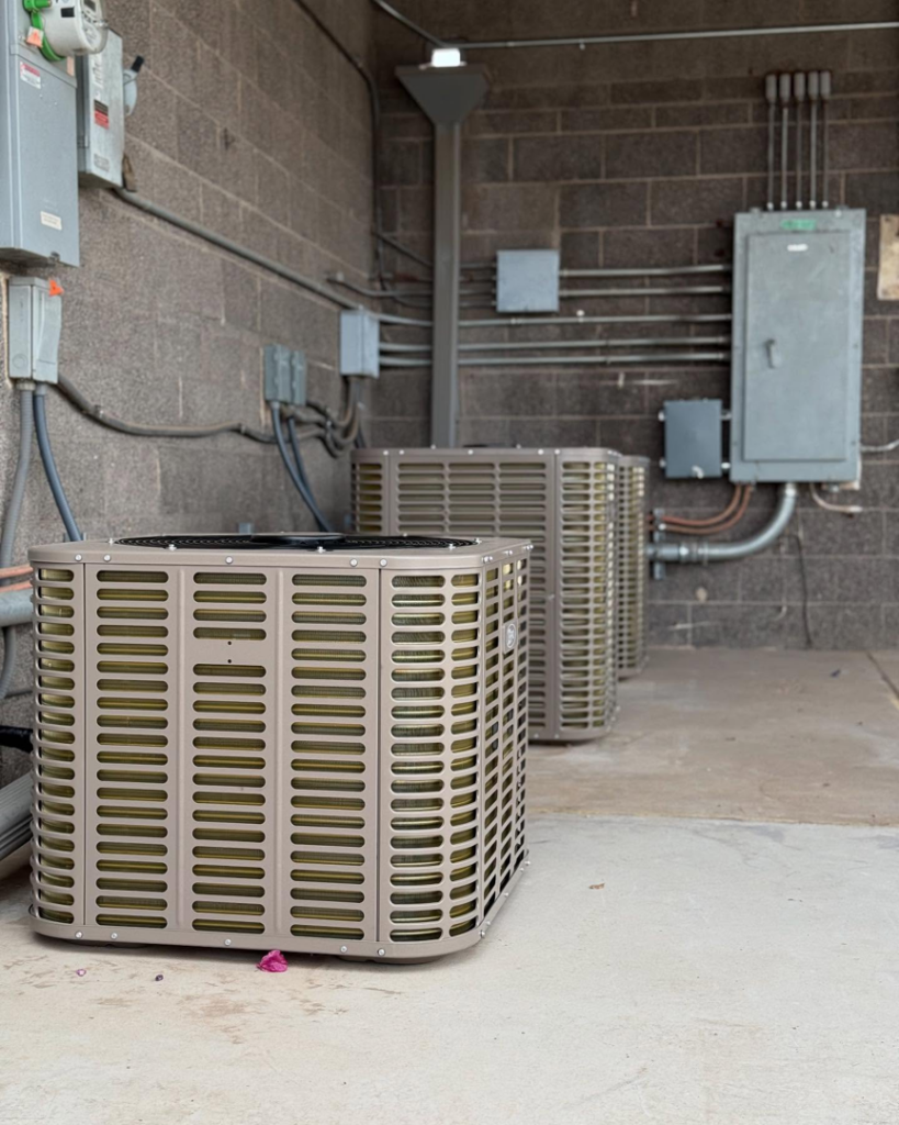 Multiple outdoor AC condenser units installed against a brick wall by Otto's Air Conditioning & Heating in Mesa, AZ.