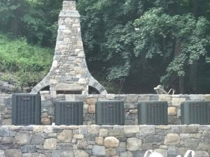 Multiple outdoor air conditioning units installed on a stone wall by Climate Care Heating & Air Conditioning in Norwalk, CT